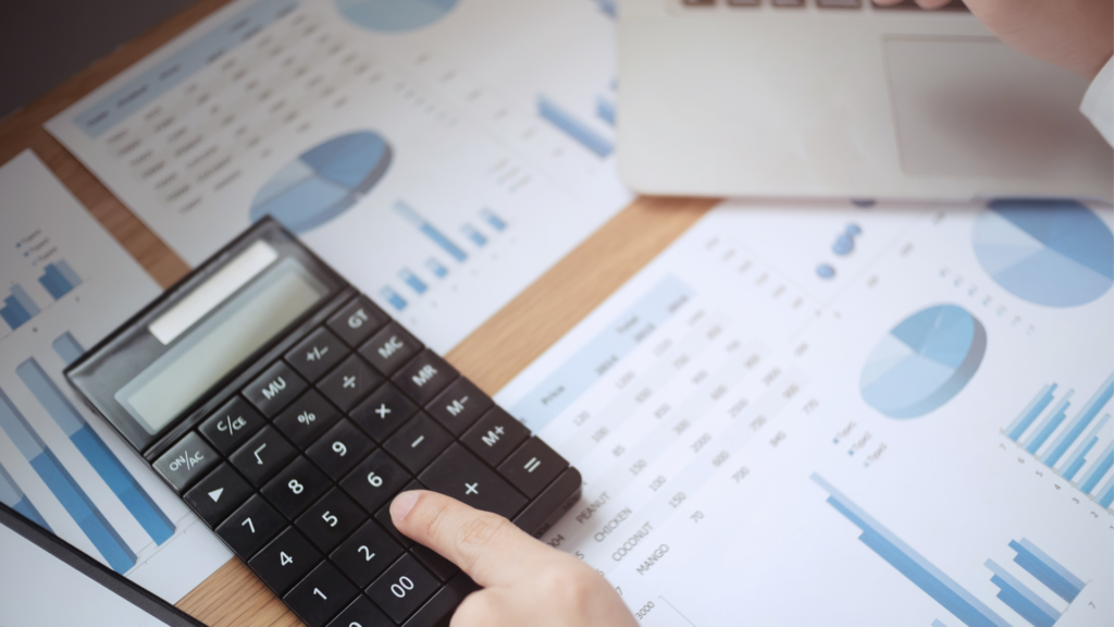 Imagem de mão com calculadora e papéis com gráficos