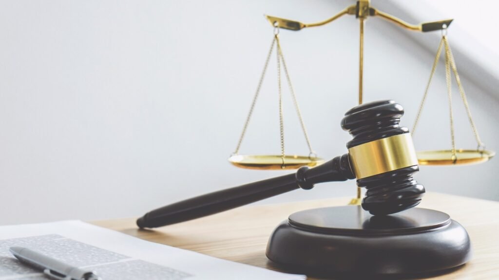imagem de um martelo de juiz em cima de uma mesa com uma balança da justiça e um papel e caneta ao lado