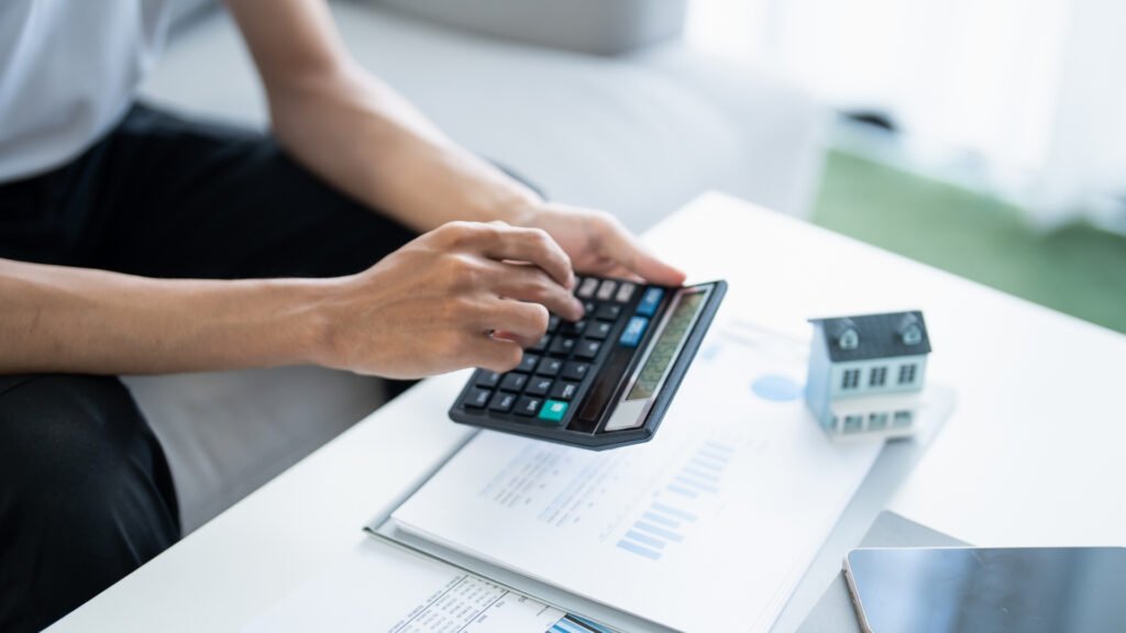 Imagem de pessoa manuseando calculadora e papeis em cima de uma mesa