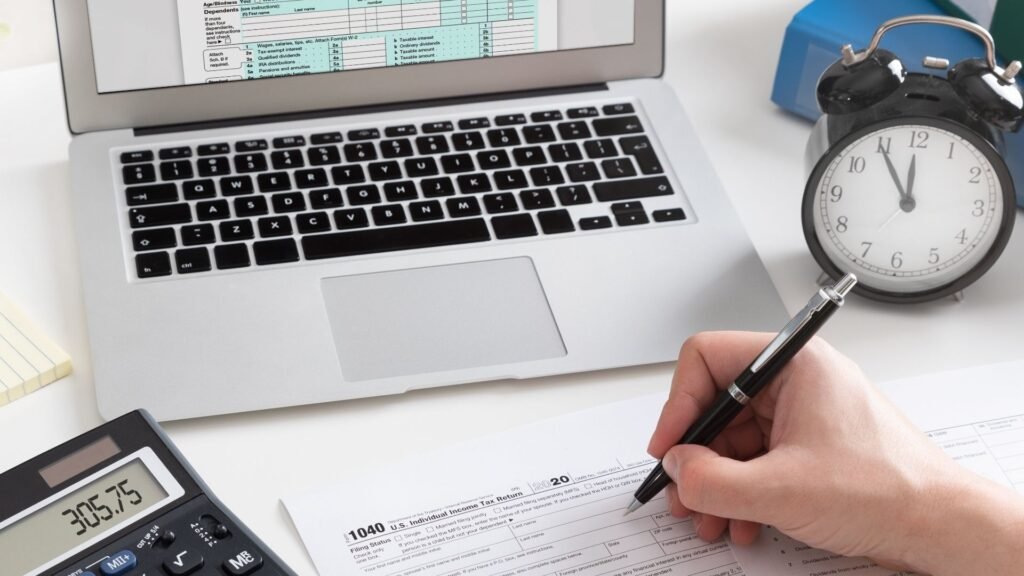 pessoa escreve em papel em frente de notebook e calculadora