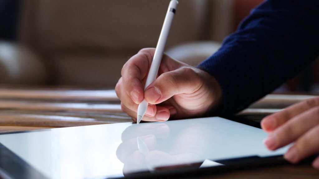 mãos manuseiam ipad com uma caneta digital