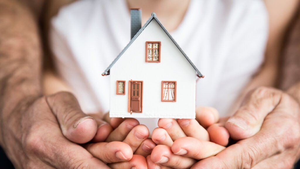 mãos de adulto e criança seguram miniatura de casa