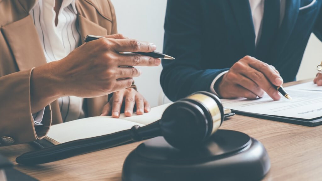 duas pessoas em mesa com papéis e martelo da Justiça