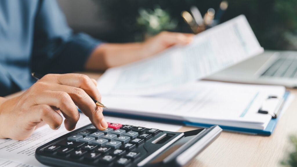 Imagem de mãos manuseando calculadora e papéis em uma mesa